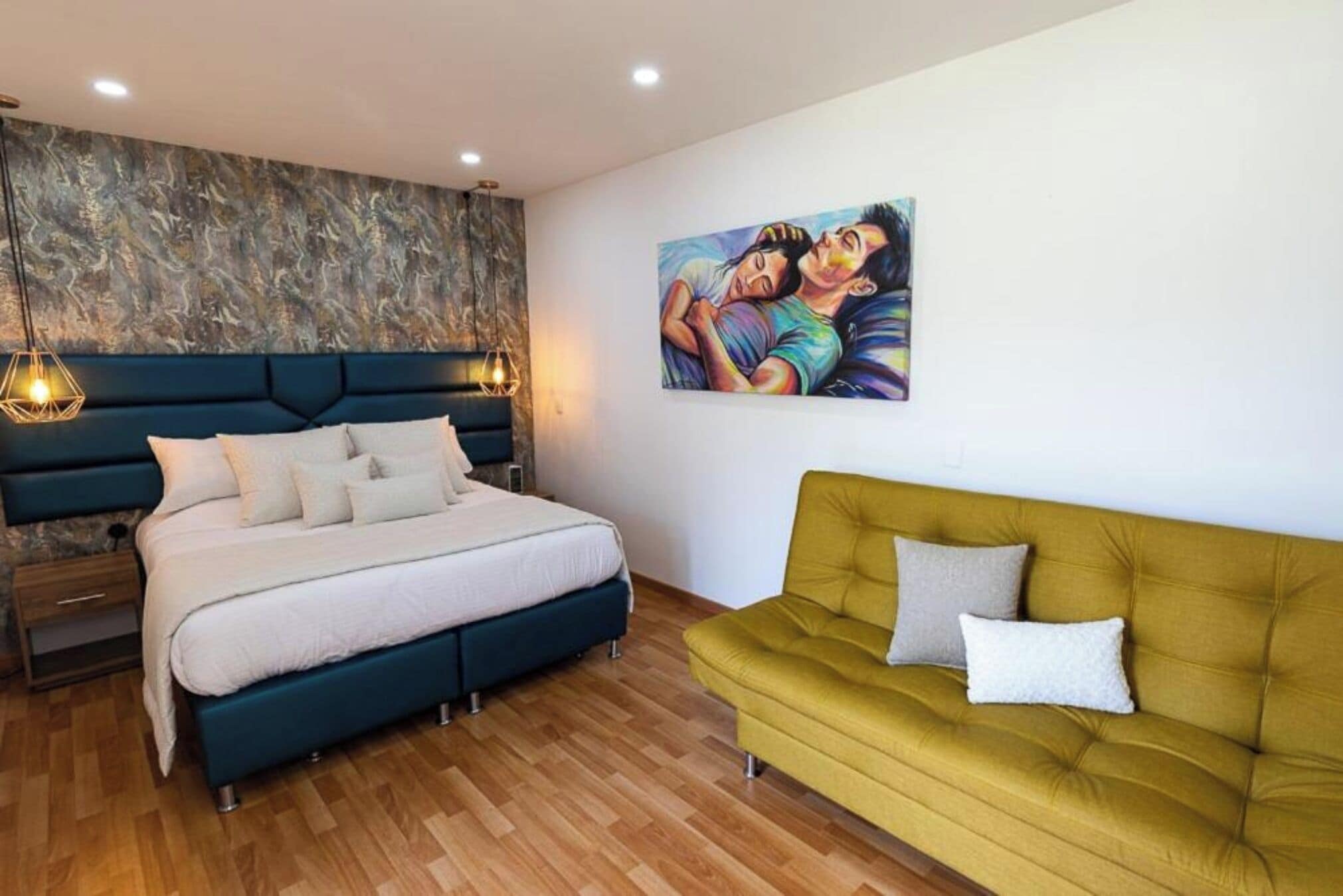 A bedroom with a bed, bedside tables, a sofa, and a painting on the wall.
