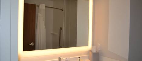 A bathroom with a large mirror, a white sink, a towel rack, and a shower visible in the reflection.