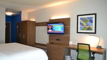 A hotel room with a bed, a desk with a computer, a TV on the wall, and a trash can.