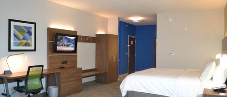 Habitación de hotel con cama, escritorio, silla, televisión, armario y puerta de baño.