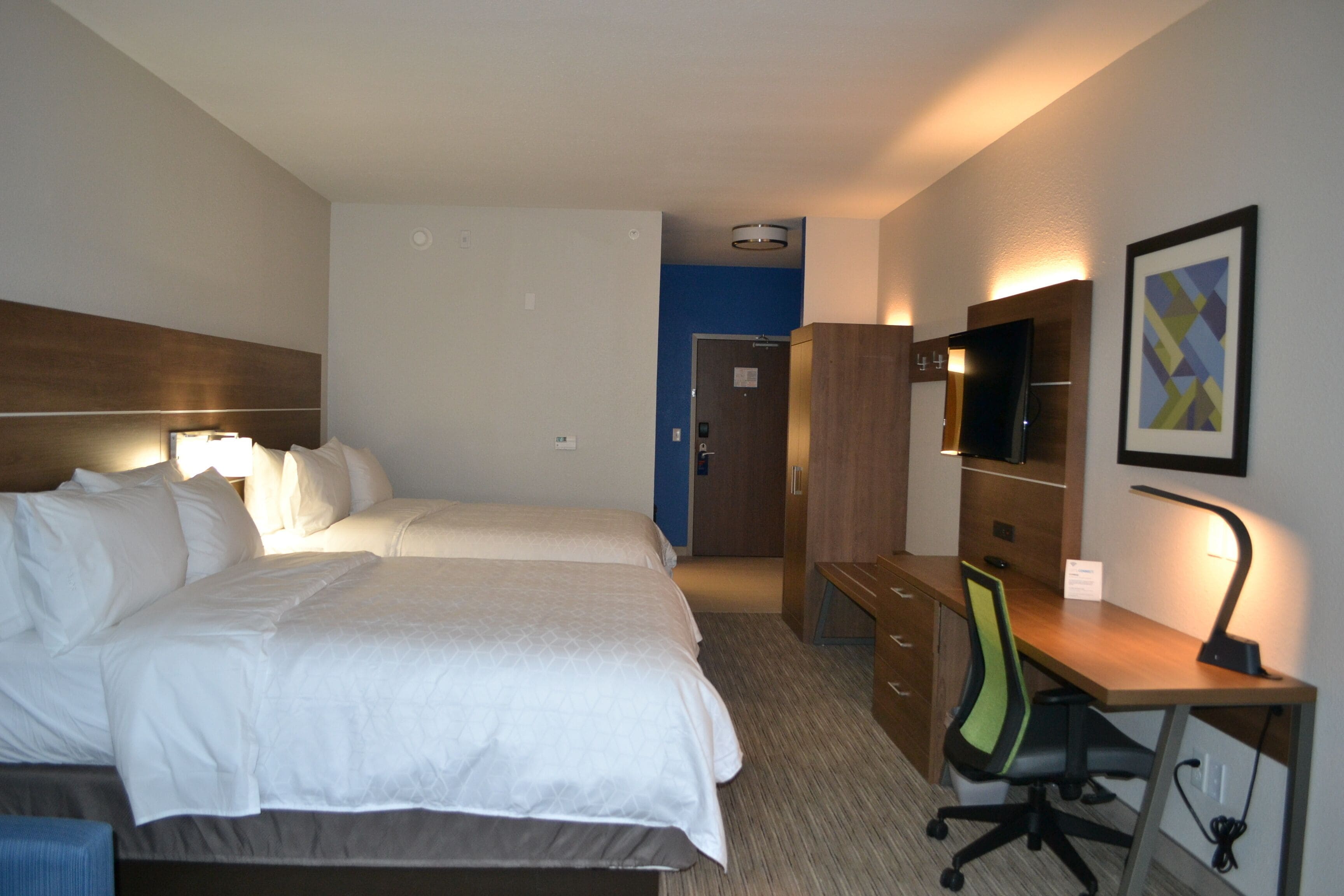 A hotel room with two beds, a desk, a chair, a TV, and a wardrobe.