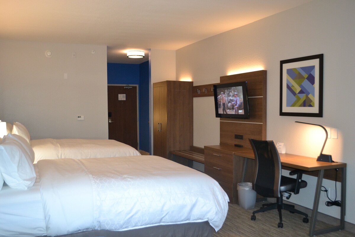 A hotel room with two beds, a desk with a computer, a TV, and a framed picture on the wall.
