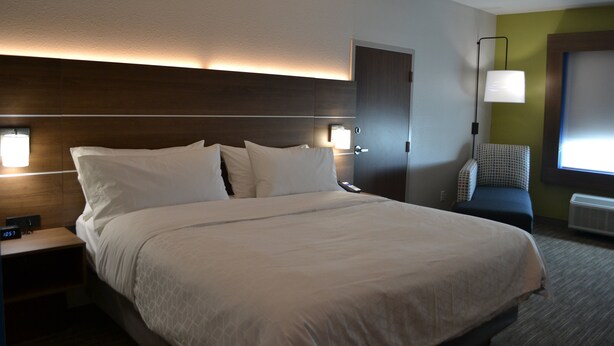 A hotel room with a large bed, bedside lamps, a nightstand, a chair, and a door. - Holiday Inn Express Tallahassee University Central by IHG (Tallahassee)