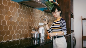 A kitchen with a hexagonal tile backsplash, stainless steel appliances, and a person holding a glass lid. - RUSTIC Home (Da Nang)