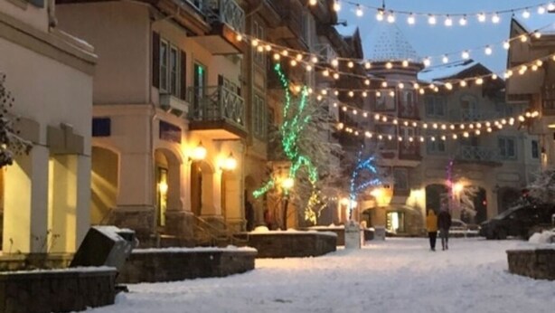 Eine schneebedeckte Straße mit Lichterketten und festlicher Dekoration, die auf eine Winterfeiertagsstimmung hindeutet.