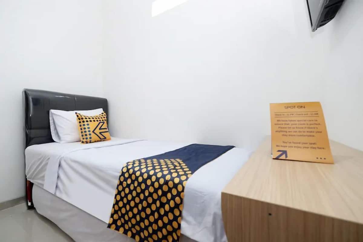 A hotel room with a bed, a wooden nightstand, a check-in sign, and a wall-mounted TV.
