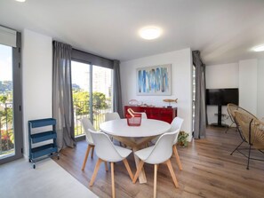 A modern dining area with a round table, white chairs, a red cabinet, and a TV.