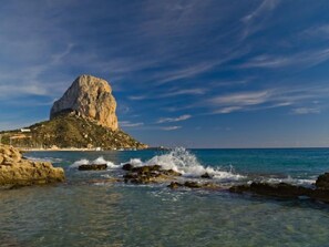 A coastal scene with a prominent rocky outcrop and clear blue waters.