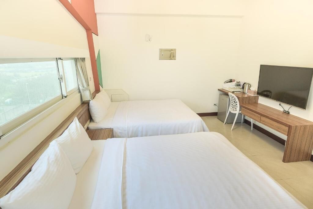A hotel room with two beds, a desk, a chair, a television, and a window.