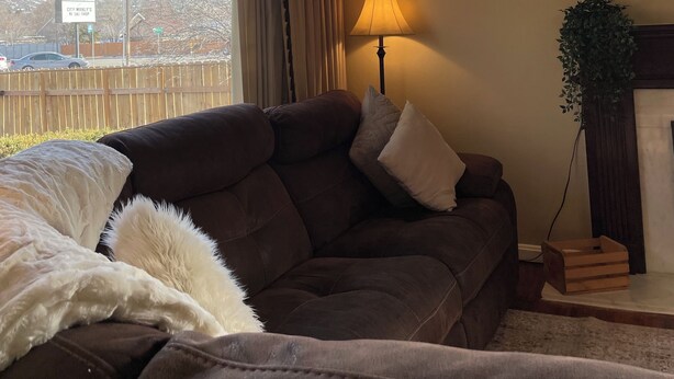Ein Wohnzimmer mit einem braunen Sofa, einer Lampe und Blick auf schneebedeckte Berge durch ein Fenster.