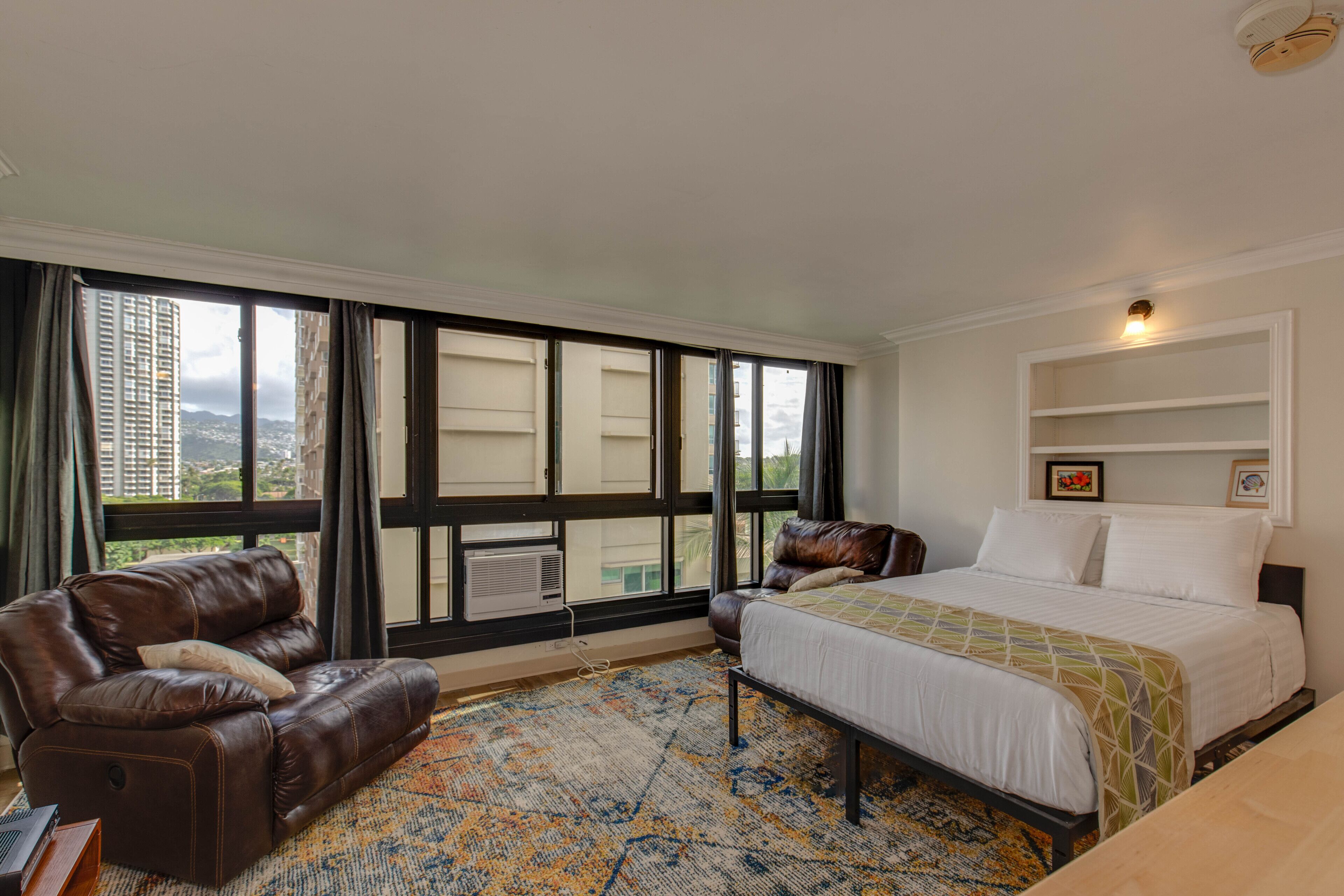 A hotel room with a large bed, a leather sofa, a window with curtains, and a view of buildings.