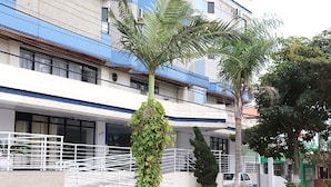 Un edificio moderno con fachada azul y blanca, una entrada con portón y una palmera en primer plano.