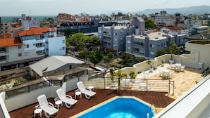 Piscina en la azotea con sillones blancos, rodeada por una terraza de madera y una barandilla de metal.