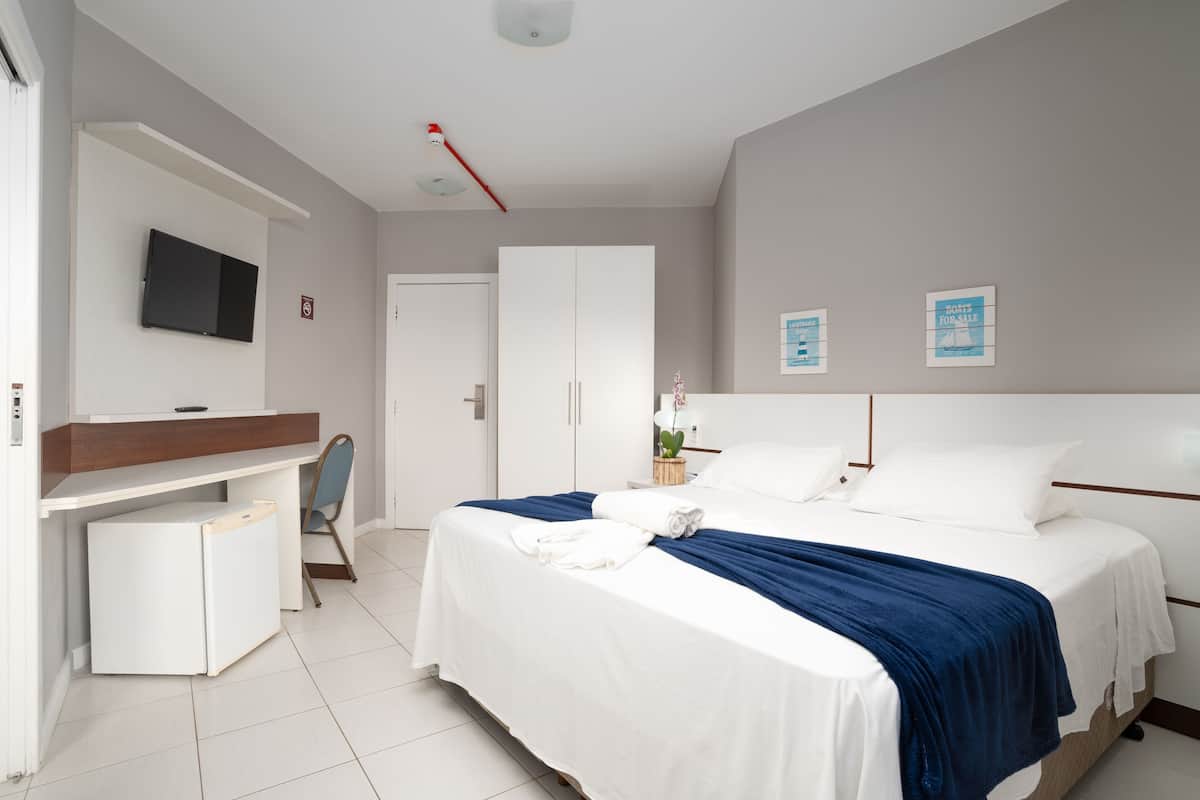 Une chambre d’hôtel moderne équipée d’un lit, d’un bureau, d’une chaise, d’une télévision et d’une armoire.