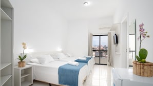 Habitación de hotel con dos camas, un armario blanco, una mesita con una planta y vista a la ciudad desde la ventana.