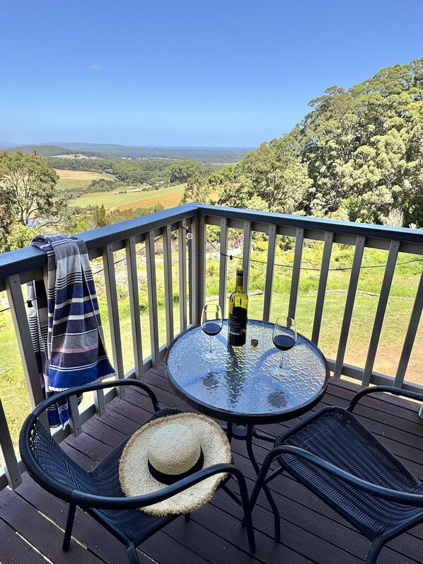 A deck with a glass table, two chairs, a bottle of wine, and a straw hat.