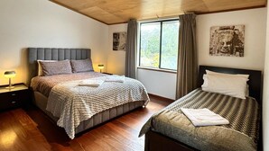 A bedroom with two beds, wooden flooring, a large window with curtains, and a ceiling with recessed lighting. - Serendeva: Private, panoramic views, dogs allowed & EV charger (Shadforth)