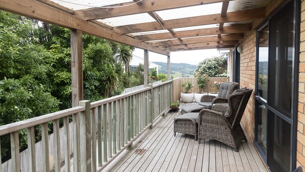Una terraza de madera con muebles de mimbre y un ventanal que da a un muro de ladrillo.