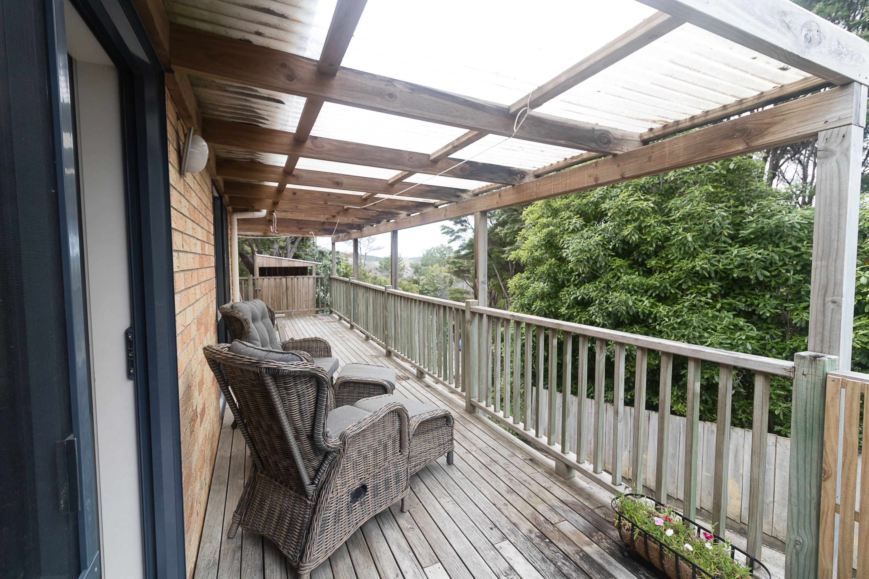 Une terrasse en bois, dotée de meubles en osier et d’une rambarde.