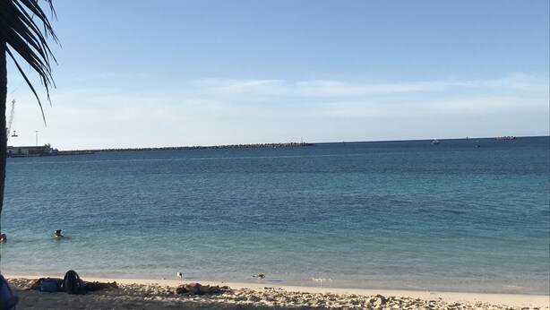Una playa con aguas azul cristalino, una orilla arenosa y un muelle a lo lejos.