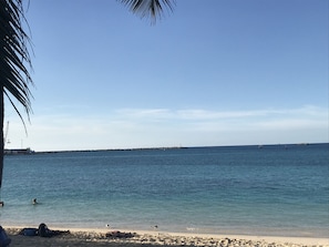 Una playa con aguas azul cristalino, una orilla arenosa y un muelle a lo lejos.
