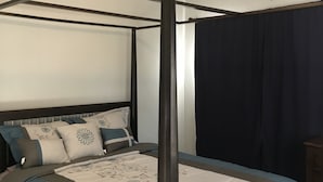 Una cama con dosel y cortinas oscuras, con ventilador de techo y una paleta de colores neutros.