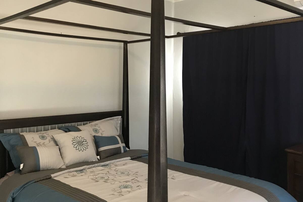 A four-poster canopy bed with a ceiling fan, dark curtains, and a neutral color scheme.