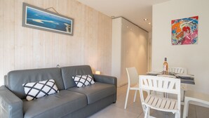 Un saló modern amb un sofà gris, cadires blanques, una taula de dinar i obres d'art a les parets.