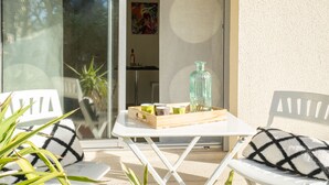 Zona d'estar exterior moderna amb caires blanques, una taula petita, una planta en test i una ampolla de vidre.