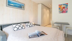 Un dormitori modern amb llit, una zona de lectura amb taula i cadires, i un quadre a la paret.
