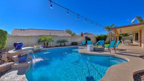 A backyard with a swimming pool, blue chairs, and a patio area. - Desert Oasis - Heated Pool, Putting Green, Lots of Parking (Gilbert)