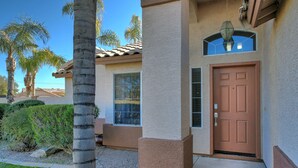 A residential building with a brown door, a small porch, and a window with a view of palm trees. - Desert Oasis - Heated Pool, Putting Green, Lots of Parking (Gilbert)