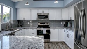 A modern kitchen with white cabinets, stainless steel appliances, and a granite countertop. - Desert Oasis - Heated Pool, Putting Green, Lots of Parking (Gilbert)