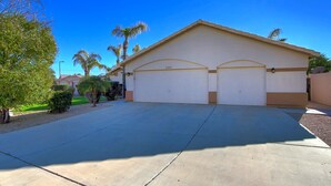 A two-story house with a garage, a well-maintained lawn, and palm trees. - Desert Oasis - Heated Pool, Putting Green, Lots of Parking (Gilbert)