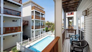 A multi-story building with a swimming pool, wooden railings, and a covered balcony area.