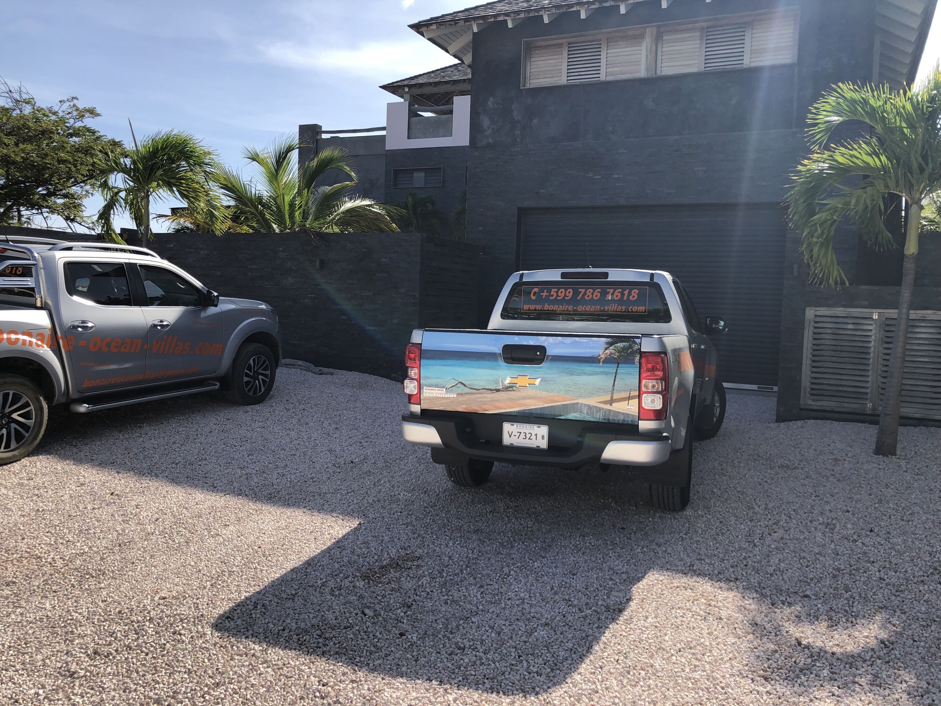 Una camioneta pickup estacionada en un camino de grava con un adhesivo decorativo de temática playera en la parte trasera.