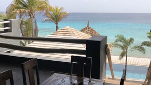 Ein Holztisch und Stühle in einer überdachten Außenbereich mit Blick auf das Meer und Palmen.