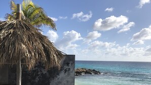 Eine Holzterrasse führt zu einem Strand mit einer Palme und einer Betonmauer.