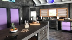 Eine moderne Küche mit einer zentralen Kochinsel, einem Kühlschrank und einem Fenster mit Jalousien.