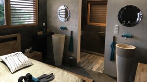 Ein modernes Badezimmer mit einem großen, runden Spiegel, einem Waschbecken und einem Fenster mit Jalousien.