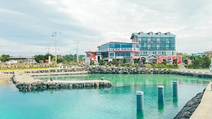 Et hotel ved vandet med en stor bygning, flere etager og altaner, en swimmingpool og en klippefyldt kystlinje.
