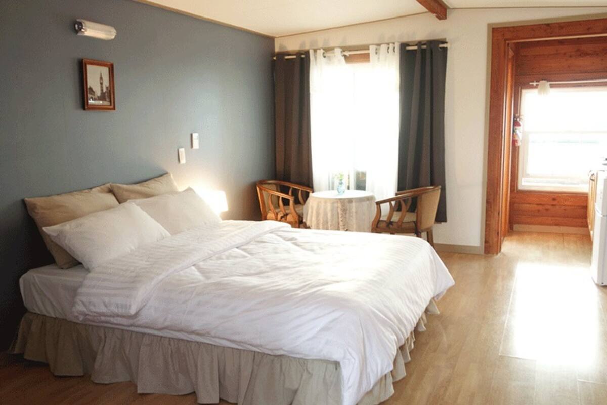A bedroom with a large bed, a small table, two chairs, and a window with curtains.