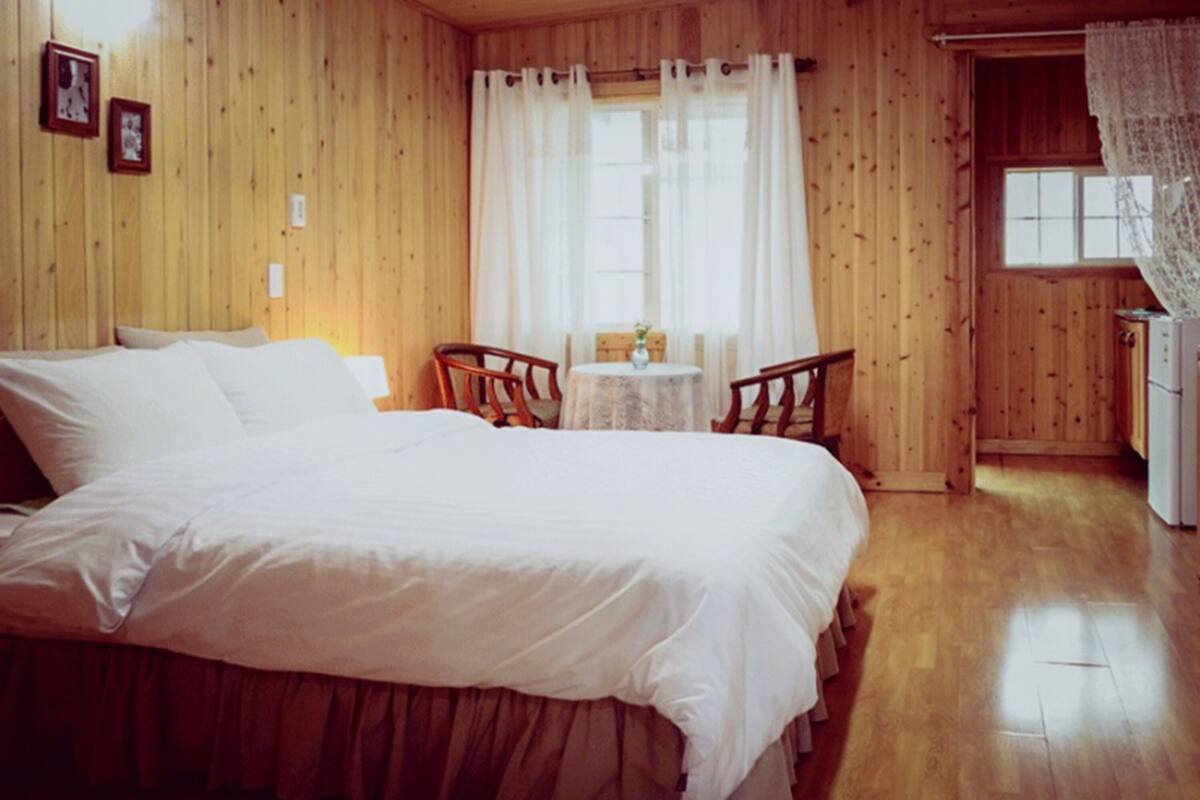 A wooden-paneled room with a large bed, a small table, and two chairs.