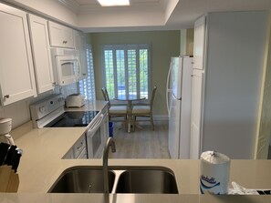 Kitchen features a double sink, stove, oven, and refrigerator, adjacent to a dining area with a table and chairs.