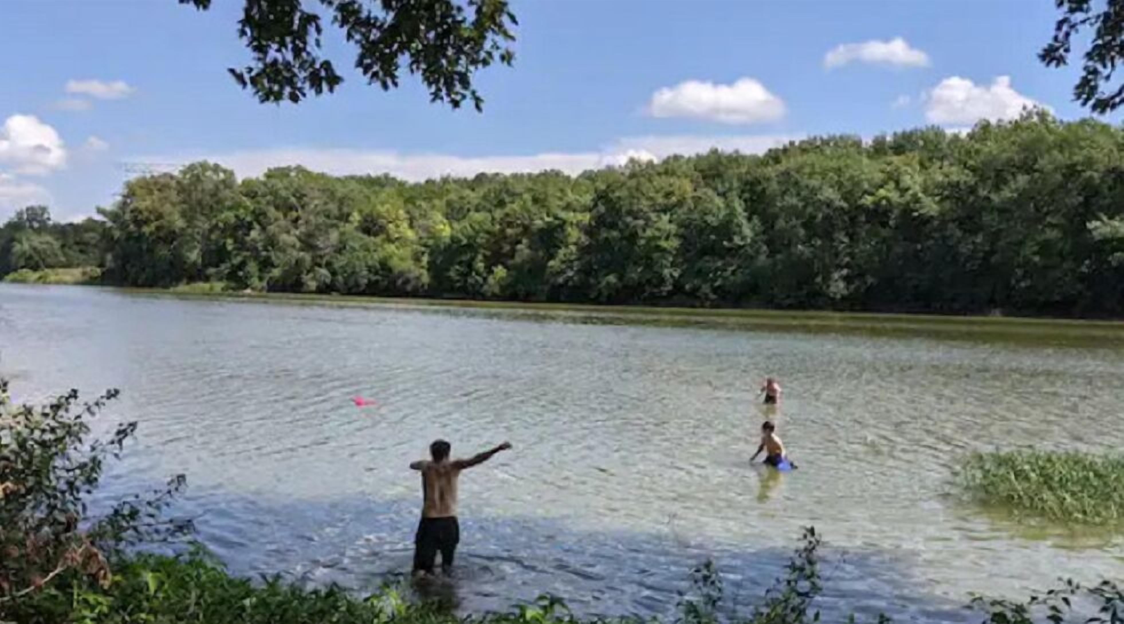 Un lago con gente nadando, rodeado de vegetación exuberante.