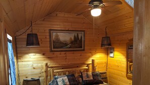 Una camera da letto accogliente in legno con un letto, una ventola a soffitto, un quadro e una botte di legno.