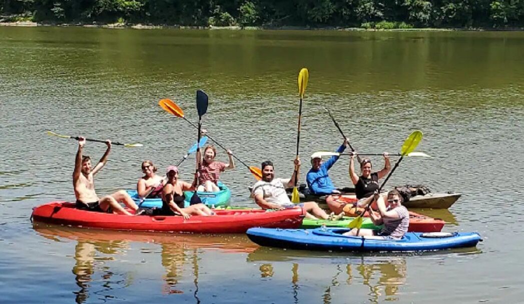 A group of people on a calm lake, paddling in colorful kayaks.