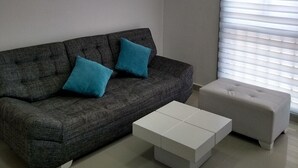 Ein modernes Wohnzimmer mit einem grauen Sofa, zwei blauen Kissen, einem weißen Couchtisch und einem grauen Hocker.