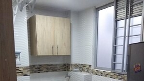 Eine kleine Küche mit Waschmaschine, einem Fenster mit Jalousien und einer gefliesten Spritzschutzwand.