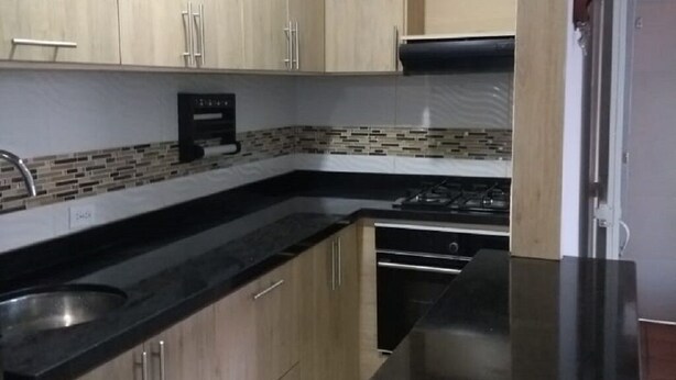Eine Küche mit Holzausstattung, einer schwarzen Arbeitsplatte und einer gefliesten Spritzschutzwand.